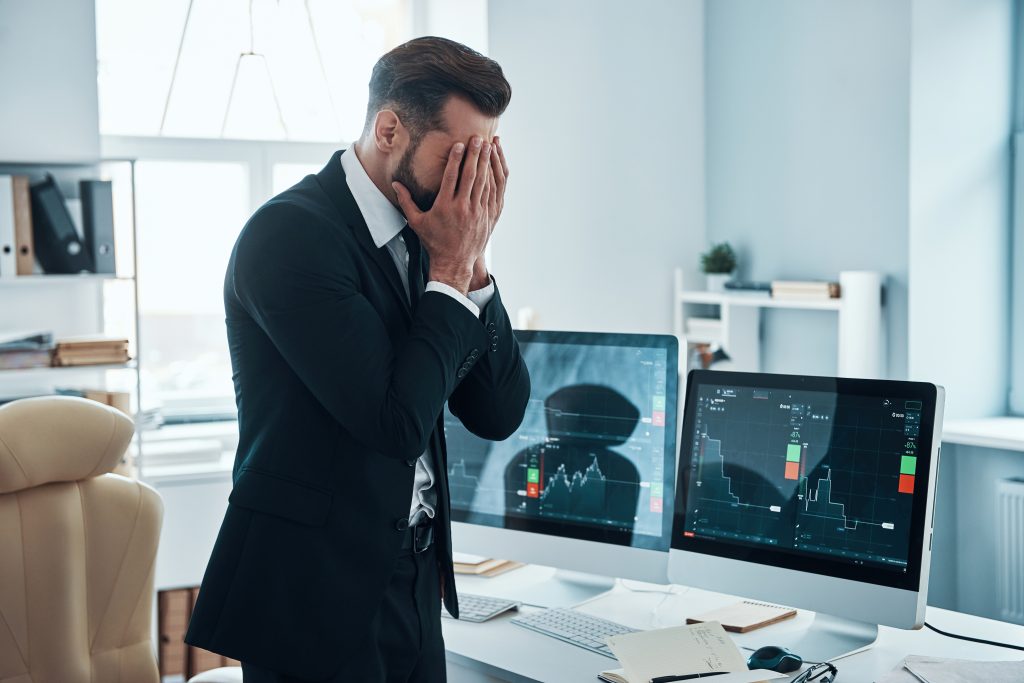 Exhausted young man in formalwear covering face with hands while working in the office